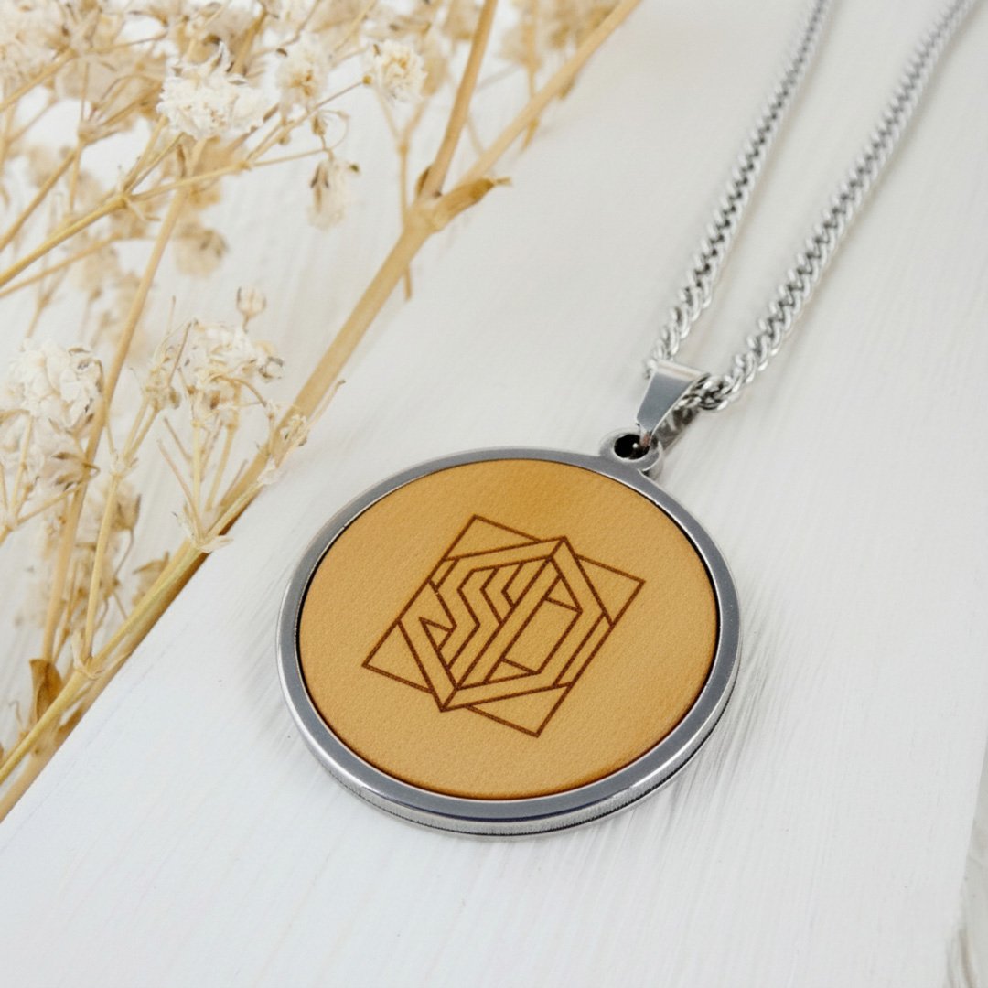 Collar personalizado con un monograma geométrico y letras estilizadas grabadas en un colgante redondo.