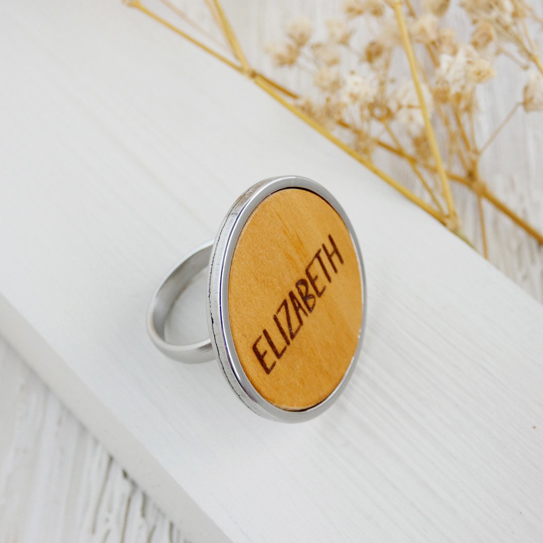 Anillo con nombre grabado en madera natural de boj y montado en una base ajustable de acero inoxidable.