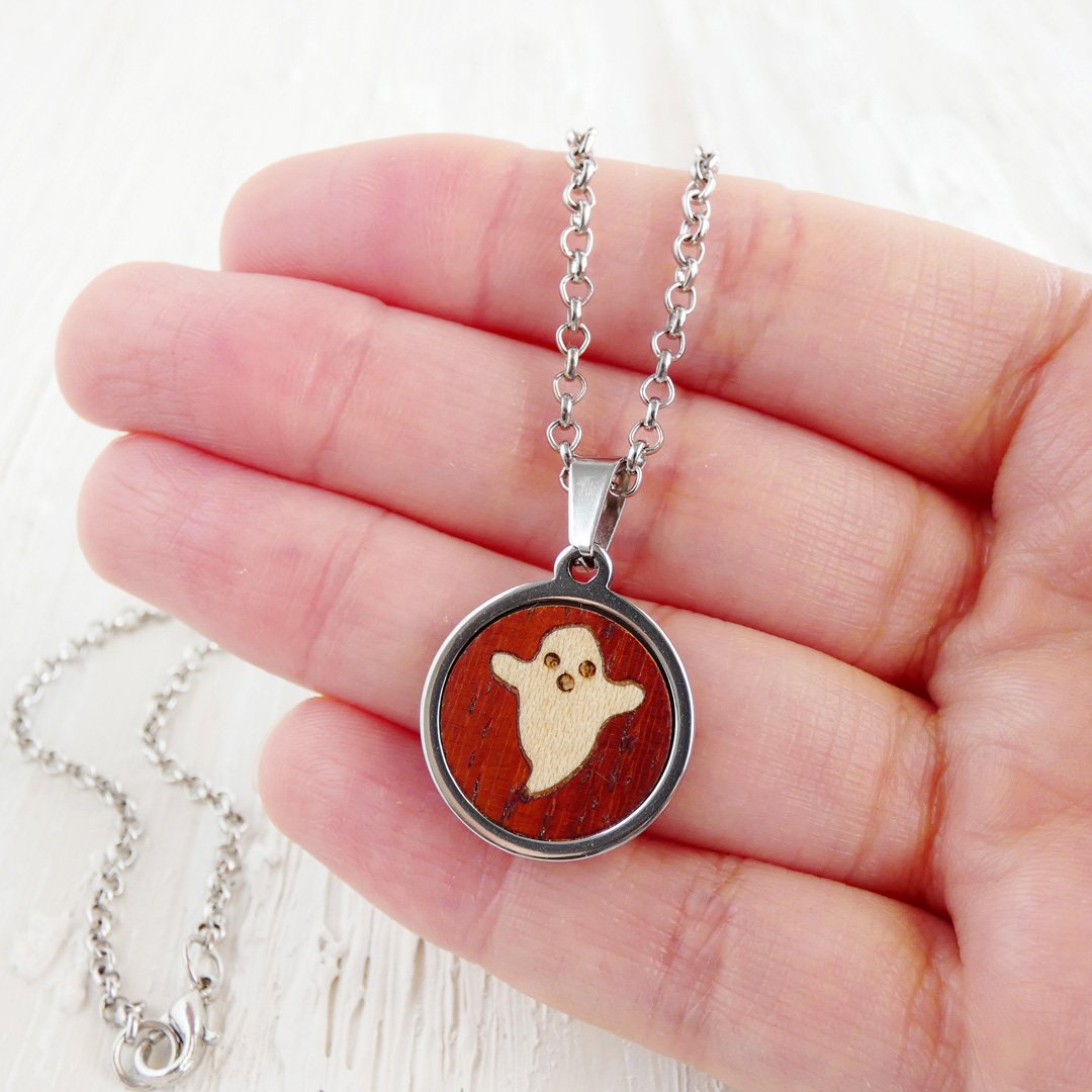 Colgante fantasma de sicomoro con marquetería artesanal y cadena de acero inoxidable mostrado en la mano