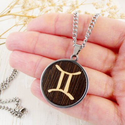 Colgante de madera de wengué Géminis mostrado en la mano para mostrar su tamaño.