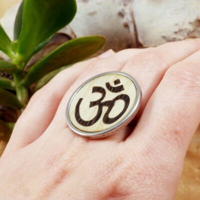 Mano de mujer llevando un anillo de madera con símbolo Om para yoga y meditación.