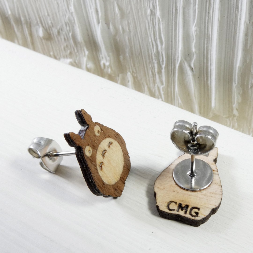 Pendiente de Totoro boca abajo mostrando las iniciales CMG grabadas en la madera