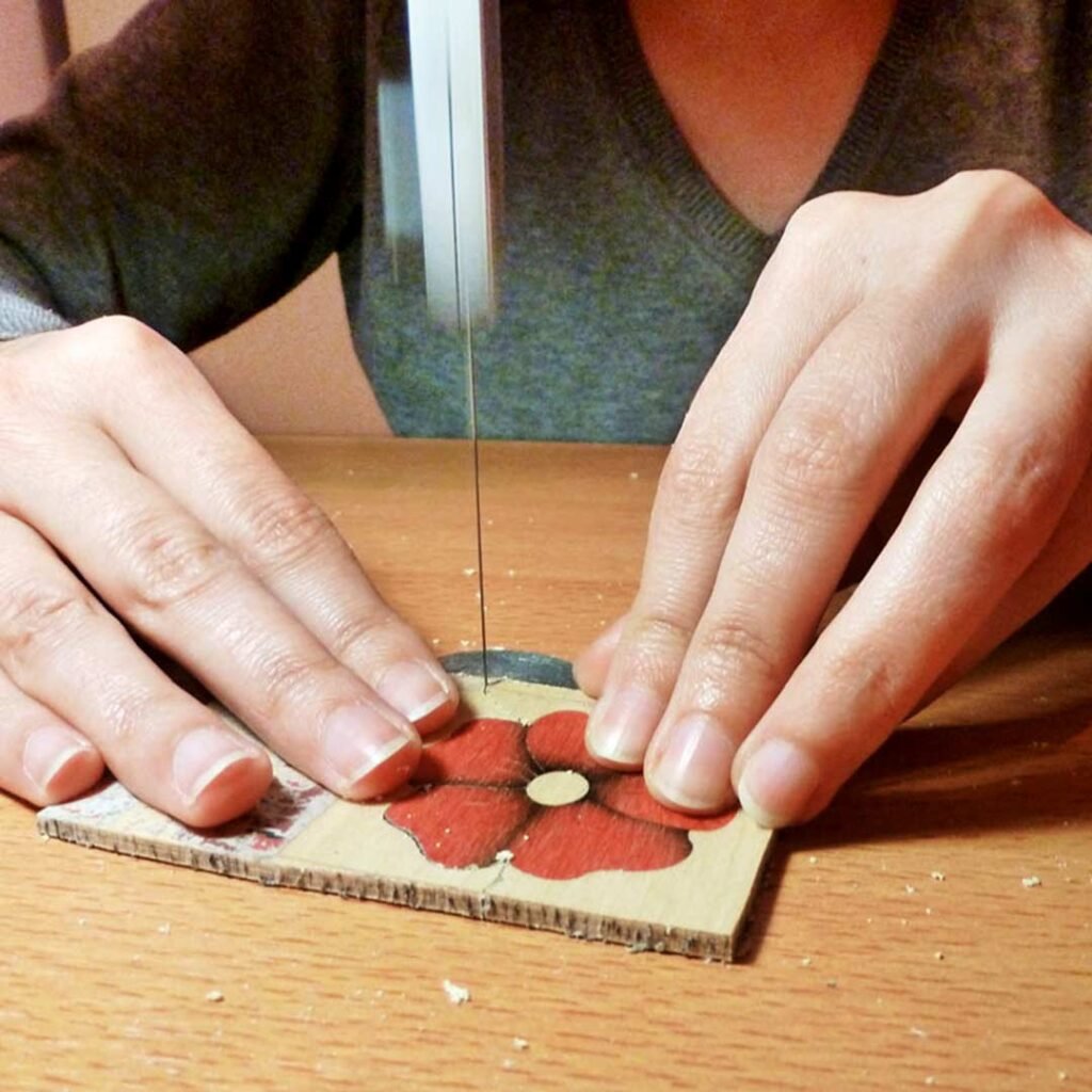 Primer plano de una artesana serrando una flor de marquetería con sierra de ballesta.
